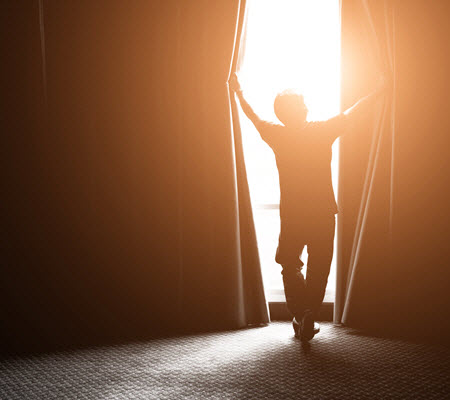An image of a man holding curtains open, representing the hope available through anxiety treatment in Richmond, VA through online therapy and counseling. | 23224 | 