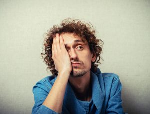 Image of a man with curly hair holding his face in his palm. This image illustrates the frustration one may experience before working with an online therapist in Virginia. You can get support from online therapy in Virginia even from Norfolk, VA. 23507 | 23503 | 23509