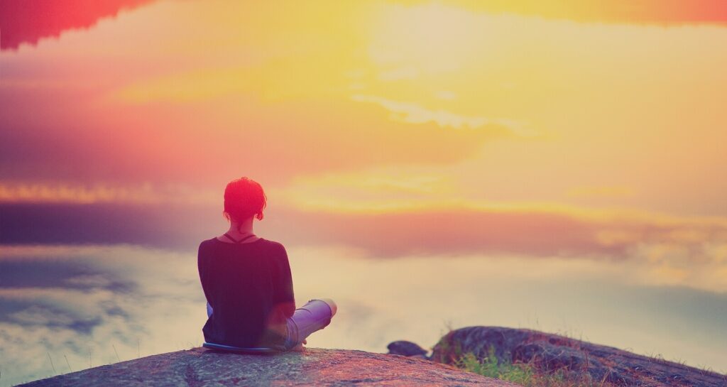 Woman sitting on an outcropping relaxing and breathing to overcome her anxiety. Anxiety does not have to control your life. Learn simple breathing techniques to calm anxiety with an onlin anxiety theraist in Virginia.