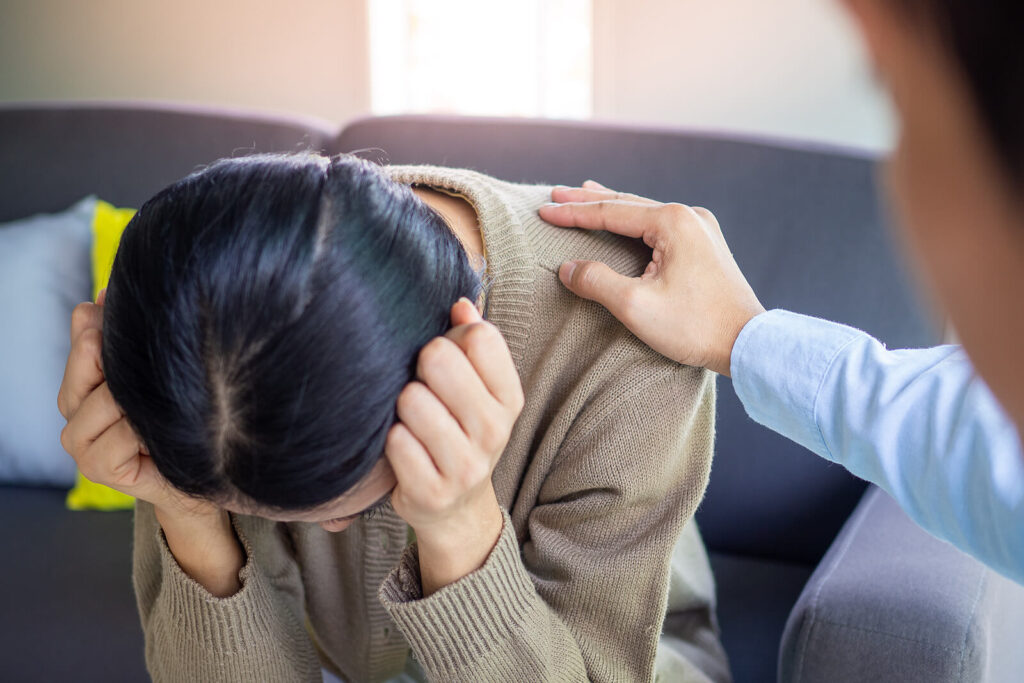 A woman hangs her head while a person offers a hand on their shoulder in support. Learn more about trauma therapy in Richmond, VA, and the support an equine sports therapist in Powhatan, VA can offer.