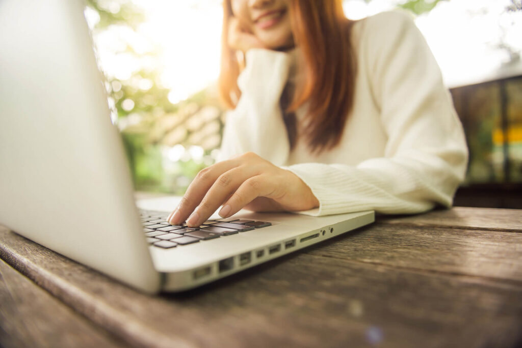 A woman smiles while typing on a laptop outside. Learn more about online therapy in Virginia and how it can address therapy for childhood trauma. An equine sports therapist in Powhatan, VA can offer support today!