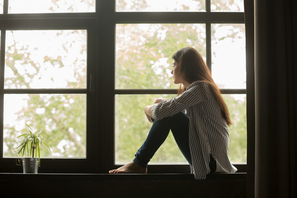 A girl sits in a window while looking outside with a stressed expression. Learn more about therapy for self-esteem in Virginia by contacting an equine sports therapist in Richmond, VA today. An anxiety therapist in Richmond, VA can offer therapy for anxiety and other services. 