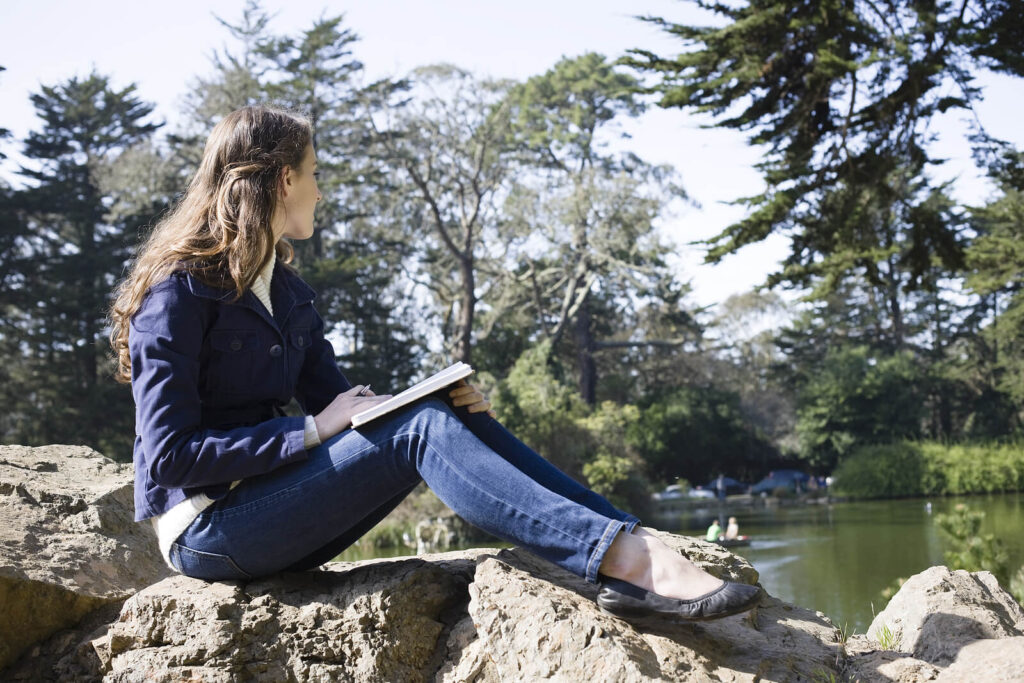 A girl sits on a rock while writing in a notebook. Learn more about coping techniques via therapy for self esteem in Virginia and how an equine therapist in Powhatan, VA can offer support via therapy for anxiety and more. 