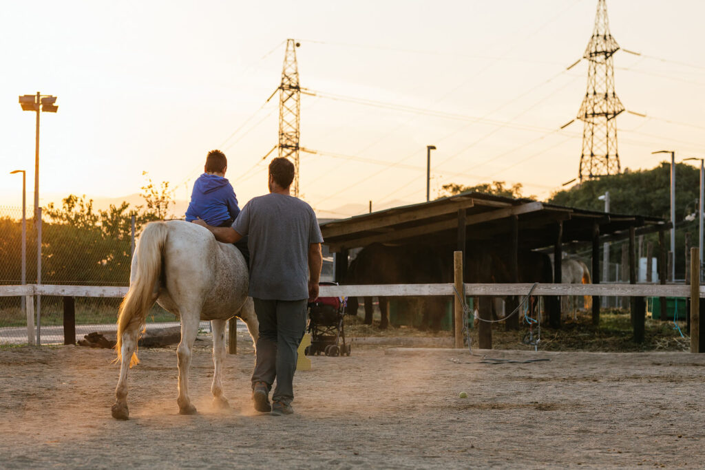 A person walks along a horse with a child on its back. This could represent the support an equine therapist in Virginia can offer. Search for equine therapy in Virginia to learn more about equine sports therapy in Virginia today. 