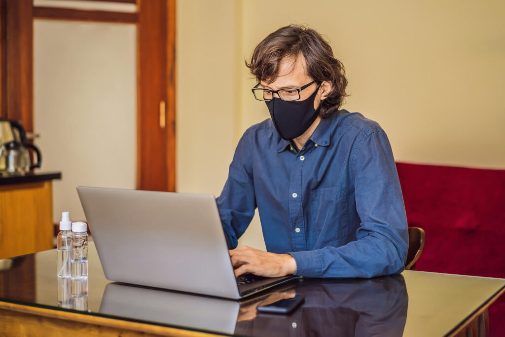 A man wearing a mask sits at a table while typing on his laptop. This could represent the convenience of online therapy in Lynchburg, VA that an equine therapist in Virginia can offer. Search for Virginia online therapy to learn more today. 