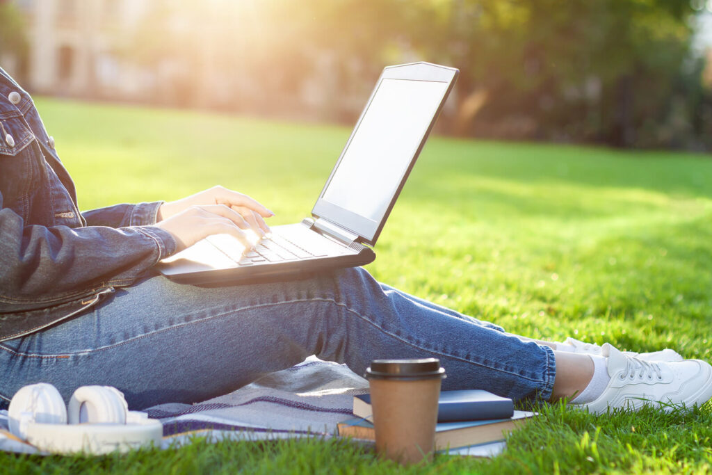 A close-up of a person typing on a laptop while sitting in the grass on a sunny day. Learn how an equine therapist in Virginia can offer support with online therapy in Virginia and other services. Search for online therapy in Lynchburg, VA, and other services. 