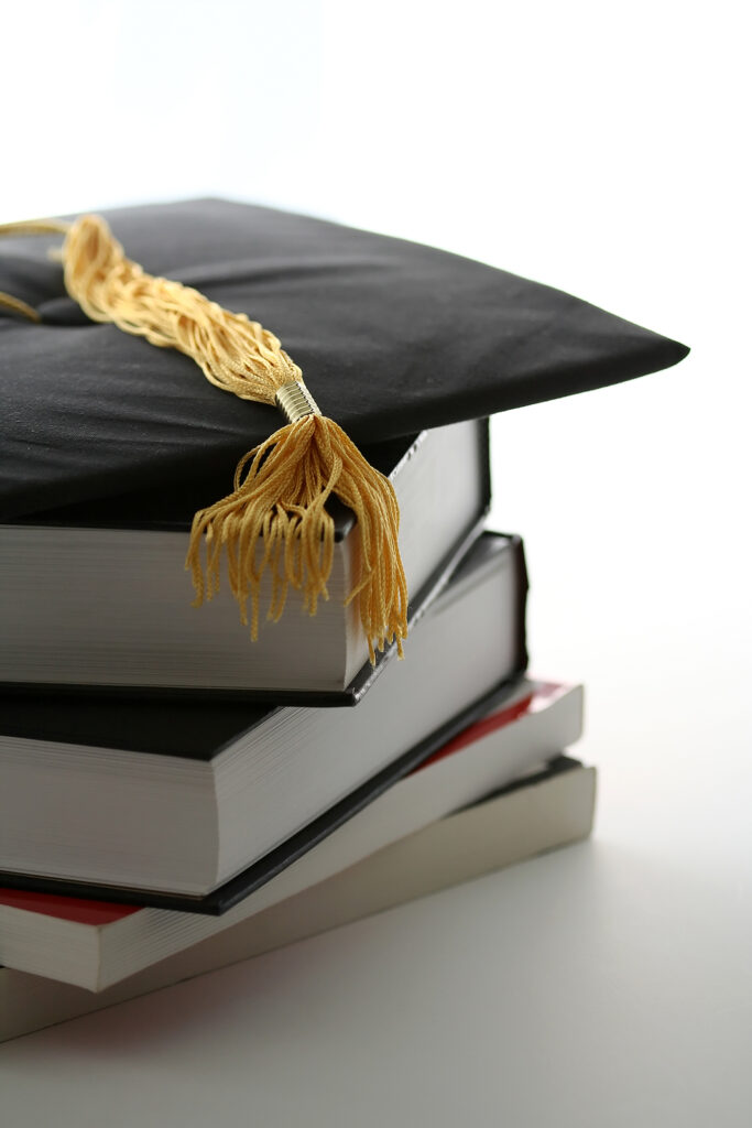 A close up of a graduation cap resting on textbooks. This could represent an expected transition that an equine therapist in Virginia can help you cope with. Learn more about online therapy in Virginia by searching for life transitions therapy in Culpeper VA today. 