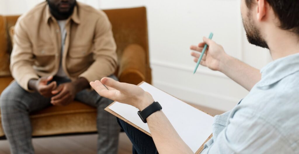 A man with a clipboard gestures with his hands while talking. This could represent the support a therapy for men in Lynchburg, VA can offer. Contact for support with men's mental health therapy in Richmond, VA or search for therapy for men in powhatan, va today. 