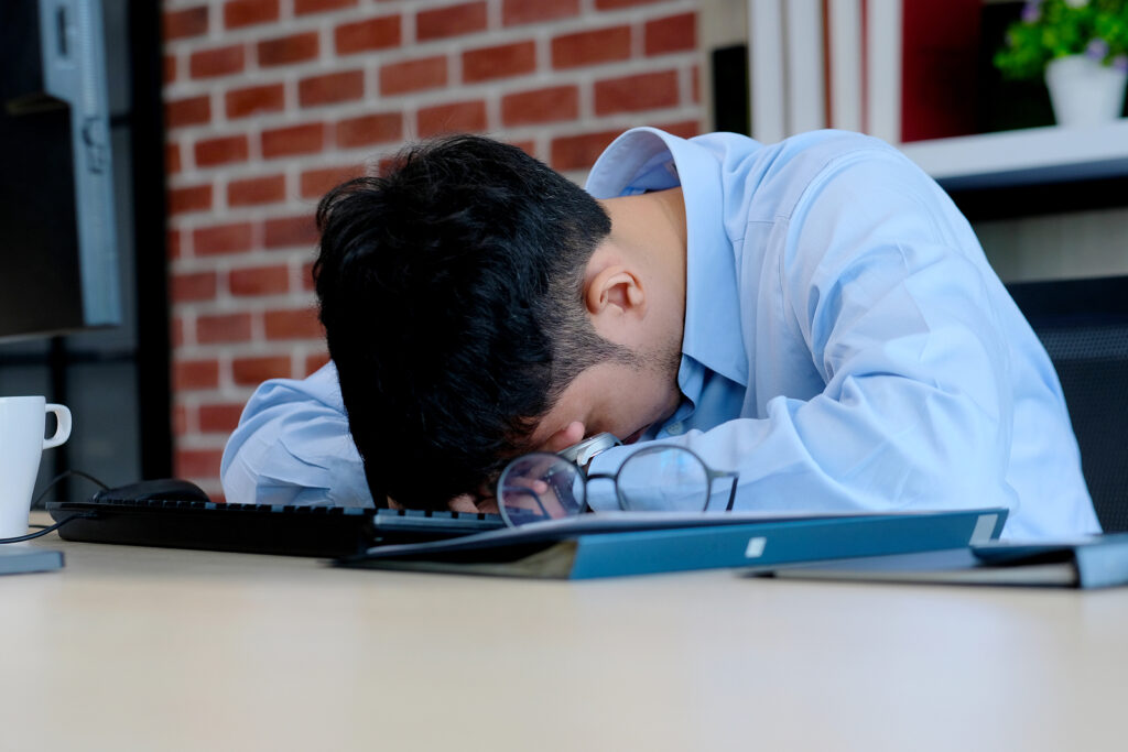 A man sits with his head down on a desk, representing the struggles men face that therapy for men in Lynchburg, VA can address. Learn more about therapy for men in Lynchburg, VA by searching for a men's counselor in Powhatan, VA and beyond. 