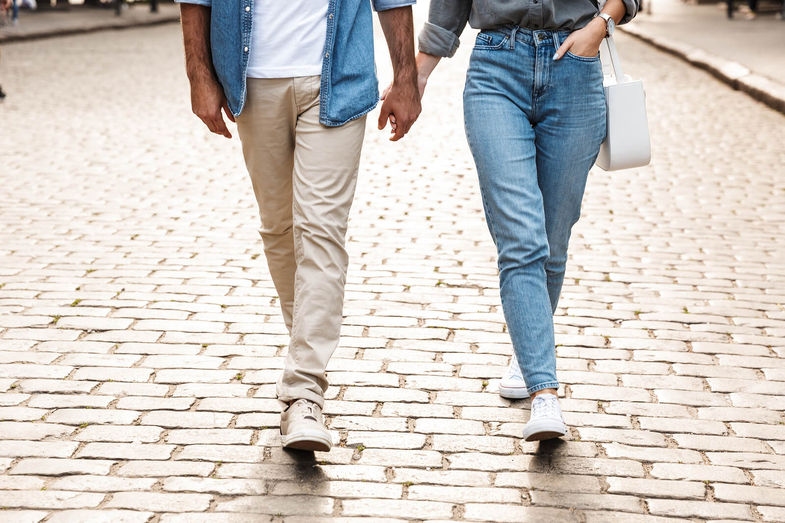 A couple holds hands while walking down a street. Learn more about the help a life transitions therapist in Fredericksburg, VA can offer with your relationship by searching for online therapy in Virginia. Search for therapy for life transitions in Virginia today.