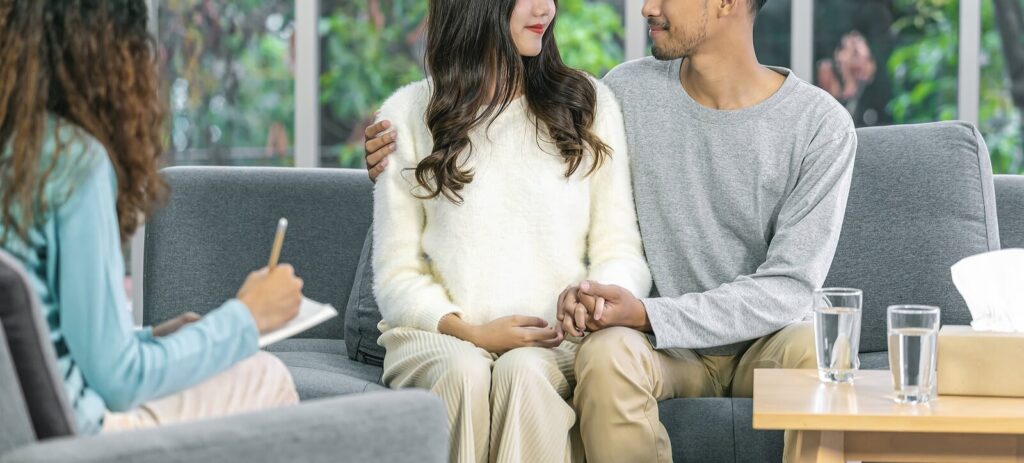 A couple smiles while sitting across a person with a clipboard. This could represent the support offered from a life transitions therapist in Fredericksburg, VA. Search for therapy for life transitions in Virginia for online therapy in Virginia. 