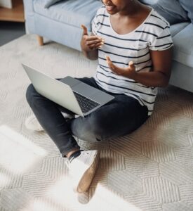 A woman gestures with her hands while talking to her laptop. She is sitting on the floor against her sofa. This could represent the ease of access for meeting with an online therapist in Powhatan, VA. Search for online therapy in Lynchburg, VA and more for remote support via online therapy in Virginia today. 