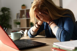 A close up of a woman covering her face while sitting at a computer desk. Learn how a depression therapist in Powhatan, VA can offer support with anxiety therapy in Powhatan, VA and other services. 