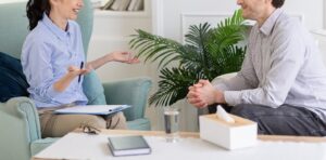 A woman with a clipboard gestures while talking to a smiling man sitting across from her. This could represent the support of an EMDR therapist in Powhatan, VA for addressing past trauma. Search for EMDR in Richmond, VA, and how therapy or EMDR intensives in Virginia can help. 