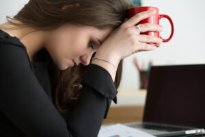 A woman rests her head on a mug at her desk, looking overwhelmed—symbolizing high-functioning anxiety in Richmond, VA and the need for support from an anxiety therapist in Richmond, VA or through online anxiety therapy in Powhatan, VA. 