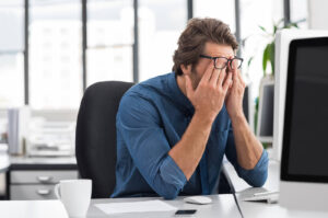 A professional man sits at his desk, covering his face in exhaustion, symbolizing burnout and hidden depression. This highlights the need for support from a depression therapist in Powhatan, VA. Accessing depression treatment in Richmond, VA or connecting with an online depression therapist in Goochland, VA can provide relief and healthier coping strategies. 