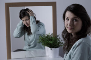 A young woman looks composed, while her reflection shows emotional distress, representing functioning depression. Many individuals seek depression treatment in Powhatan, VA to address this hidden pain. An online therapist in Powhatan, VA or depression treatment in Goochland, VA can help uncover these struggles and guide people toward healing. 