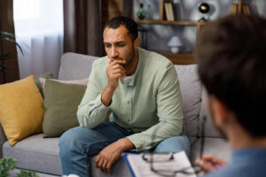 A man sits thoughtfully on a couch during a counseling session. This image represents the supportive role of a trauma therapist in Powhatan, VA, as well as the effectiveness of EMDR therapy in Richmond, VA. Working with an experienced EMDR therapist in Richmond, VA helps clients process trauma with care. 