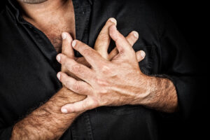 Man clutching his chest in distress against a dark background, illustrating panic symptoms that can be treated through trauma therapy in fredericksburg, va, support from a trauma therapist in richmond, va, care from an online anxiety therapist richmond, va, and guidance from an anxiety therapist in richmond, va. 