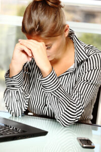 Woman with her head in her hands at a desk, representing overwhelm and nervous system shutdown. Therapy for trauma in richmond va and trauma therapy in richmond, va can support healing, whether you work with a trauma therapist new kent va or a trauma therapist in richmond, va. 