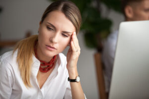 A woman sits at her desk pressing her fingers to her temple, visibly overwhelmed by stress and tension. Physical symptoms like headaches and fatigue are common ways trauma shows up in the body, something a trauma therapist in Powhatan, VA understands deeply. Recognizing these signs is often the first step toward healing through trauma therapy in Richmond, VA or with a local specialist. 