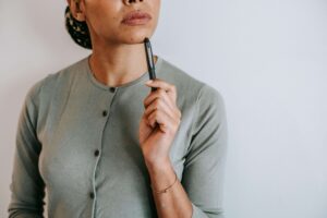 A woman holds a pen to her chin with a thoughtful, upward gaze, clearly weighing something carefully in a moment of quiet consideration. This reflective pause mirrors what many people experience before reaching out to an EMDR therapist in Richmond, VA — wondering whether they are ready, which format fits their life, and what healing might actually look like for them. An EMDR therapist in Powhatan, VA can help answer those questions through a thorough consultation before any commitment is made. 