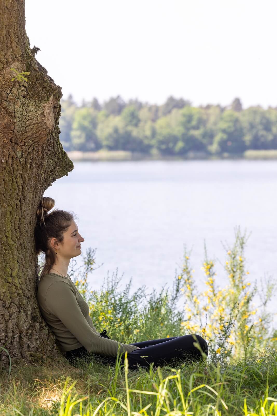 A woman sits peacefully against a tree by a lake, reflecting on her healing journey through EMDR intensives in Richmond VA with Gray Horse Counseling