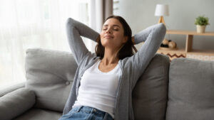 A woman leans back on the couch with her eyes closed and hands behind her head, fully at ease, the kind of relief that can follow real trauma processing. Searching emdr intensives near me or connecting with an emdr therapist in Richmond, VA or trauma therapist in Powhatan, VA can help you get there. 