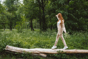 A woman walks lightly along a fallen log in a green forest, arm raised to the sun, reflecting the lightness clients often feel after an EMDR intensive Powhatan, VA or EMDR intensives Hanover, VA. An EMDR therapist in Richmond, VA can help you get there too. 