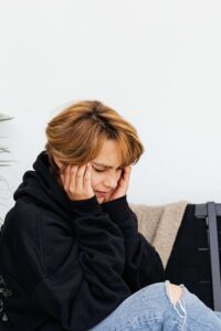 A young woman sits with her hands pressed to her temples, looking overwhelmed and tense. Hypervigilance like this is a well-trained alarm system, not weakness, whether a parent was an overt narcissist or quietly covert. A narcissism therapist in Richmond, VA offers therapy for children of narcissistic parents to help that alarm finally quiet. 