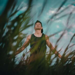 A young man stands among tall grass with his arms open and eyes closed, breathing deeply beneath an open sky. Moments of ease like this are the goal of narcissism therapy in Richmond, VA. With an online therapist in Powhatan, VA, narcissism therapy in Powhatan, VA helps you take up space and feel at home in yourself. 