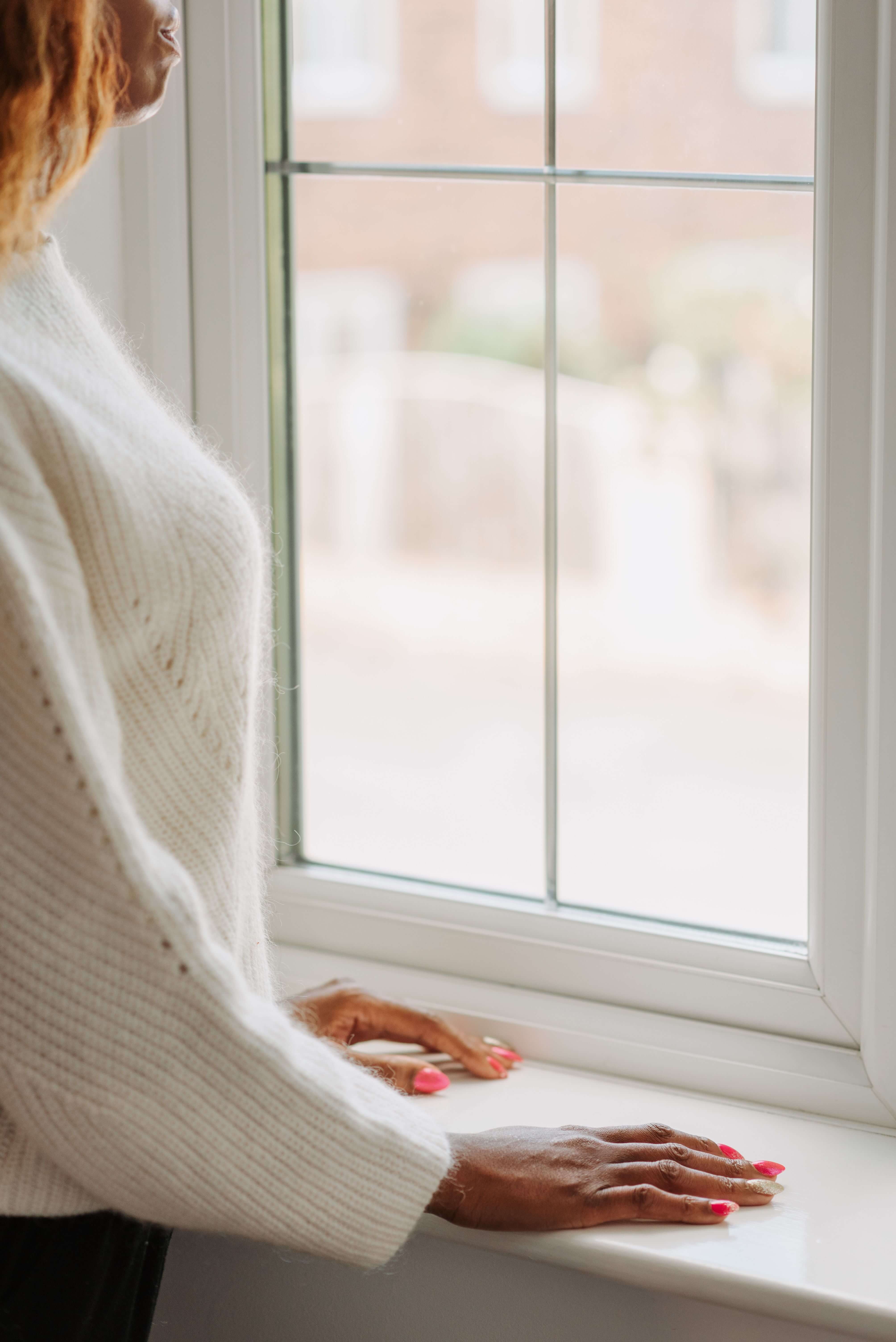 A woman in a cream sweater rests her hands on a windowsill and gazes outside, looking calm and settled. Moments of relief like this are what intensive EMDR therapy in Richmond, VA works toward. Clients considering EMDR in Richmond, VA often find these EMDR intensives in Virginia help them move forward feeling lighter. 