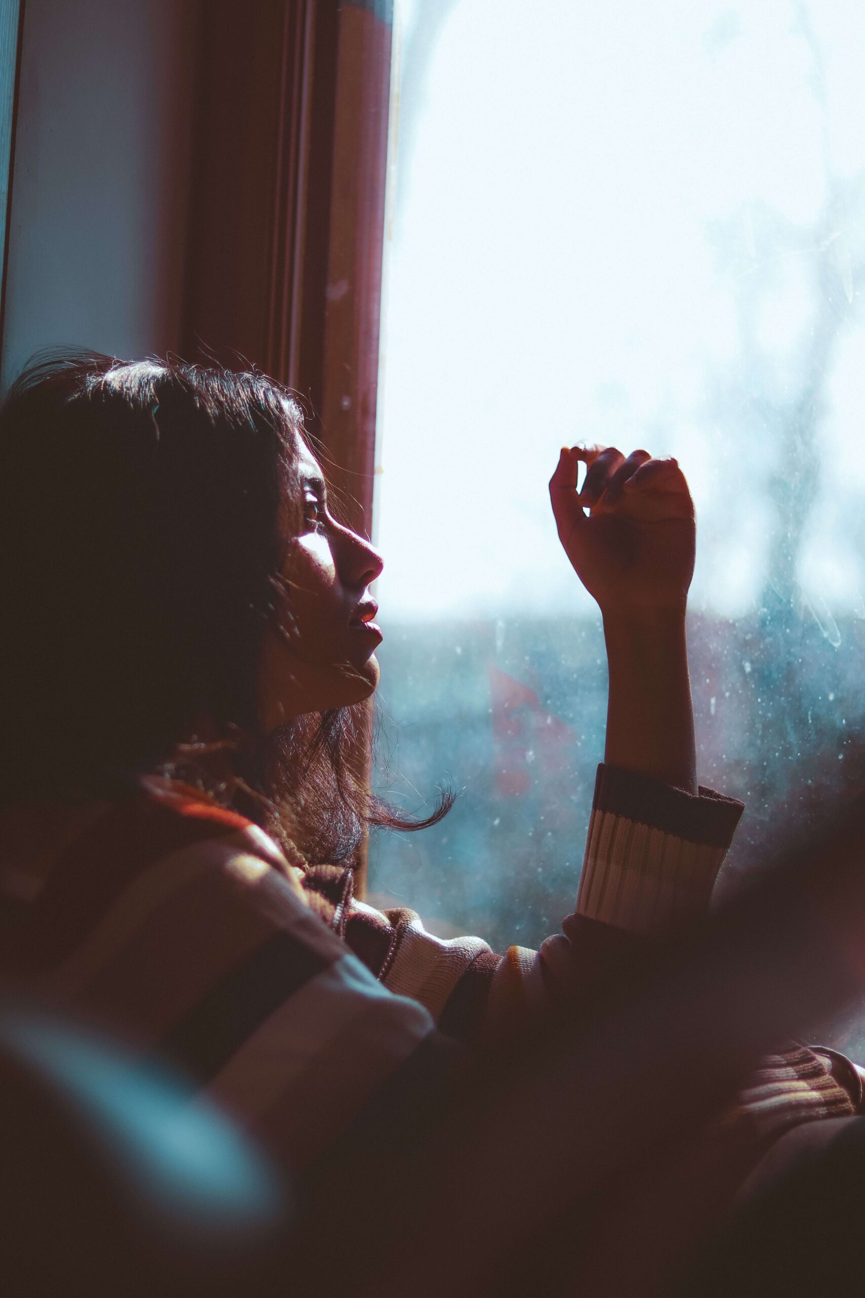 A woman sits by a bright window in warm light, looking out in a thoughtful, reflective moment. Recognizing how a childhood shaped you is the first step, and narcissism therapy in Powhatan, VA can help. Therapy for children of narcissistic parents, available with an online therapist in Powhatan, VA, helps your nervous system feel safe again.